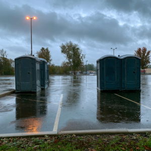 Four standard porta potties in a wet parking lot